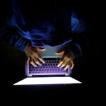 Hooded hacker silhouette with binary code background