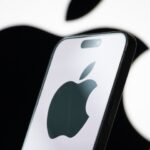 Apple logo displayed on a smartphone screen with stock market graphs in background