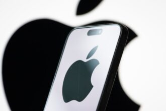 Apple logo displayed on a smartphone screen with stock market graphs in background
